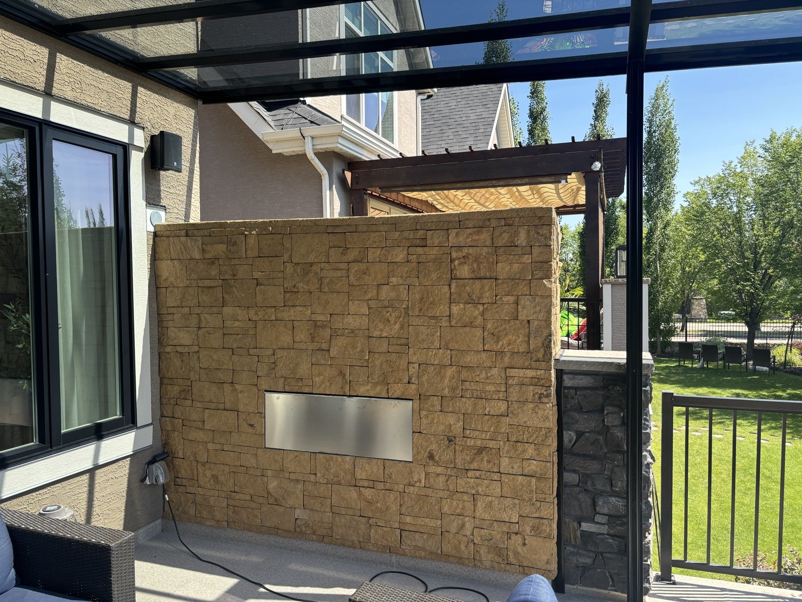Outdoor stone-clad fireplace wall with stainless steel linear insert on a covered patio